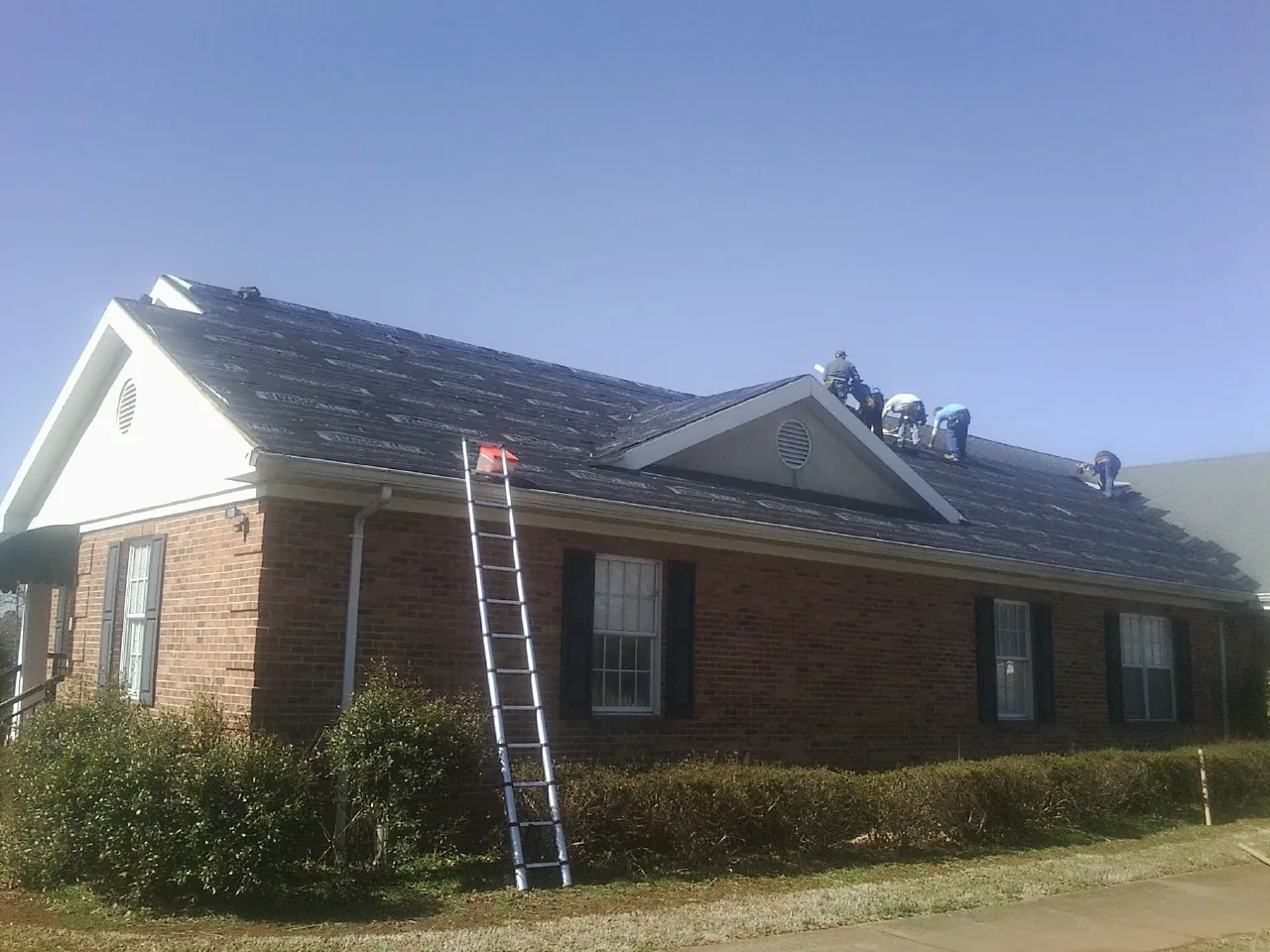 Crew tearing shingles off a brick ranch roof with a ladder set — Metal Roof Repair work by our crew in Sullivan